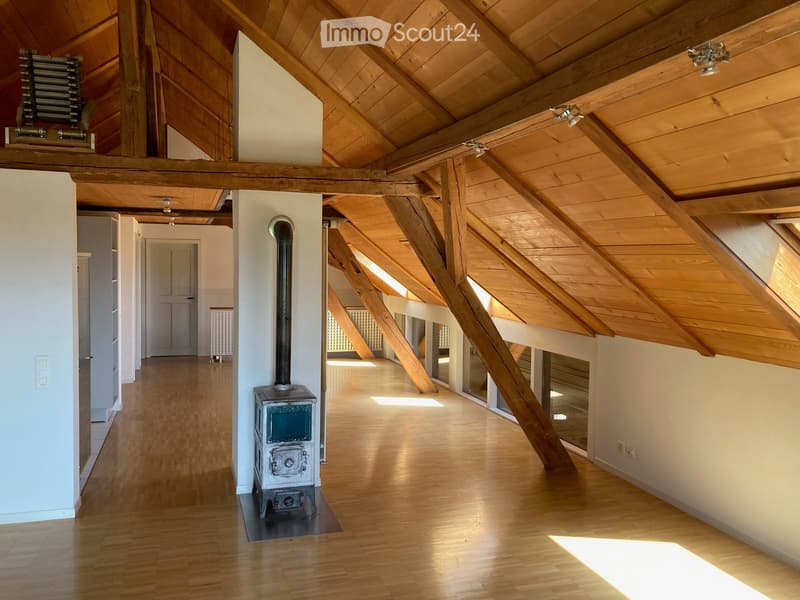 Bright, airy hallway with wooden floors and exposed wooden beams, featuring a wood-burning stove and large windows allowing natural light to flood the space.