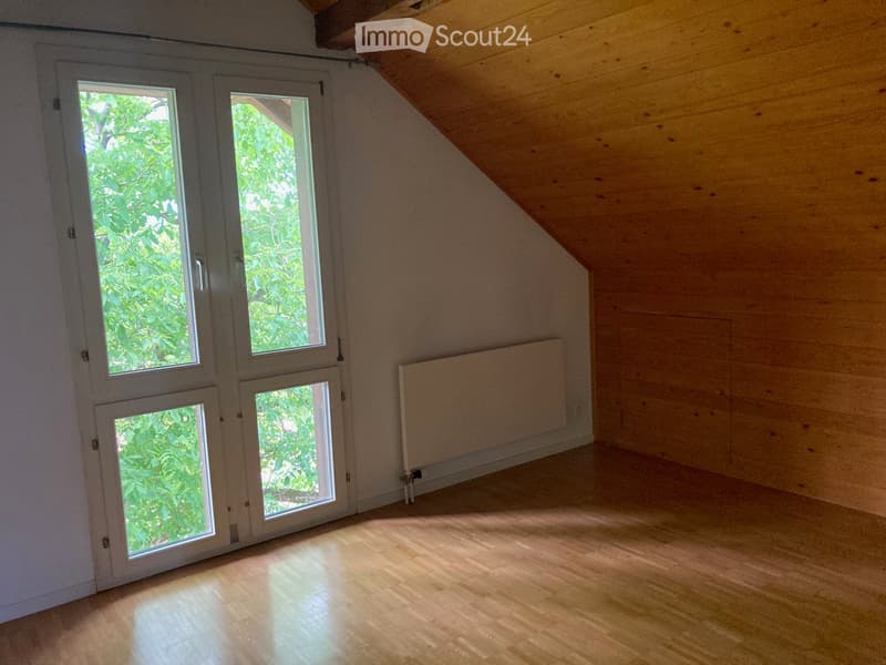 Empty attic room with wooden floors, white walls, large windows, and a radiator. No furniture or equipment present.