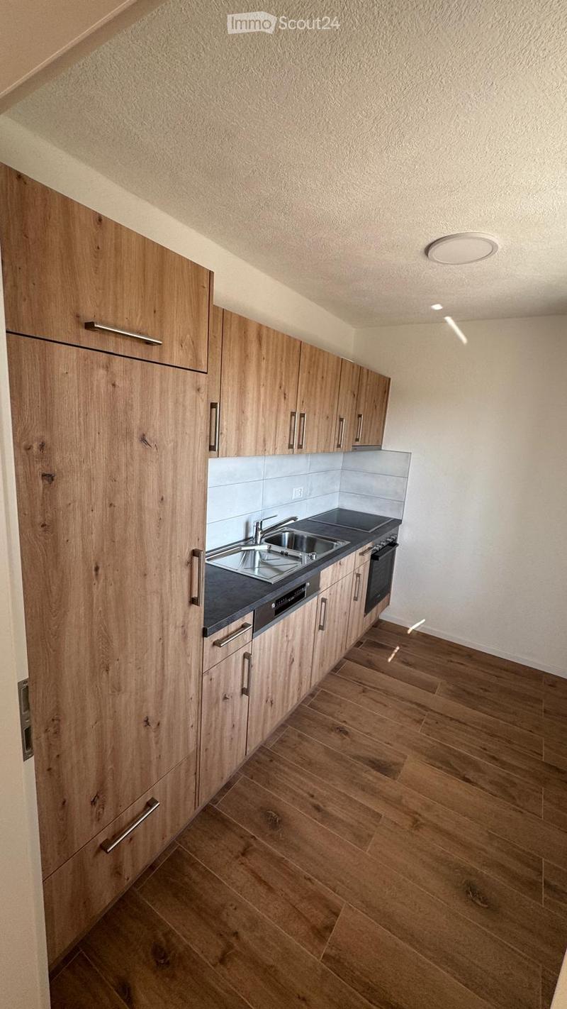 Modern kitchen with wooden cabinets, stainless steel sink, and oven. Light-colored walls and wooden flooring.