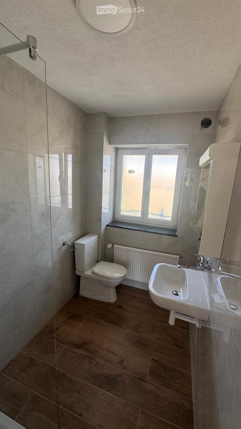 Modern bathroom with a toilet, sink, radiator, and large window. Features a glass shower enclosure and a round skylight.