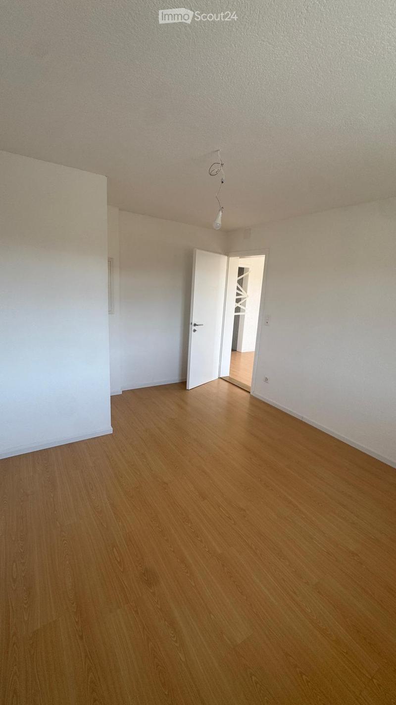 Empty room with wooden flooring, white walls, and a single open door leading to another room.