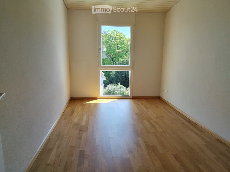 Empty room with wooden flooring and large windows letting in natural light. The walls are painted in a light neutral color, and the space appears clean and uncluttered.