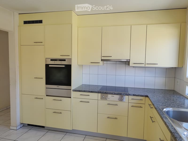 Modern kitchen with light yellow cabinets, granite countertops, stainless steel oven, and sink.