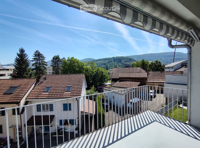 Balcony overlooking a residential area with houses, trees, and a distant mountain view.