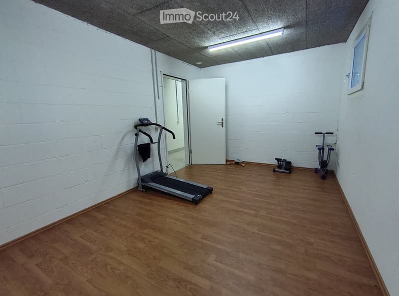 Exercise room with wooden flooring, white brick walls, a treadmill, an exercise bike, and a door leading to another space.