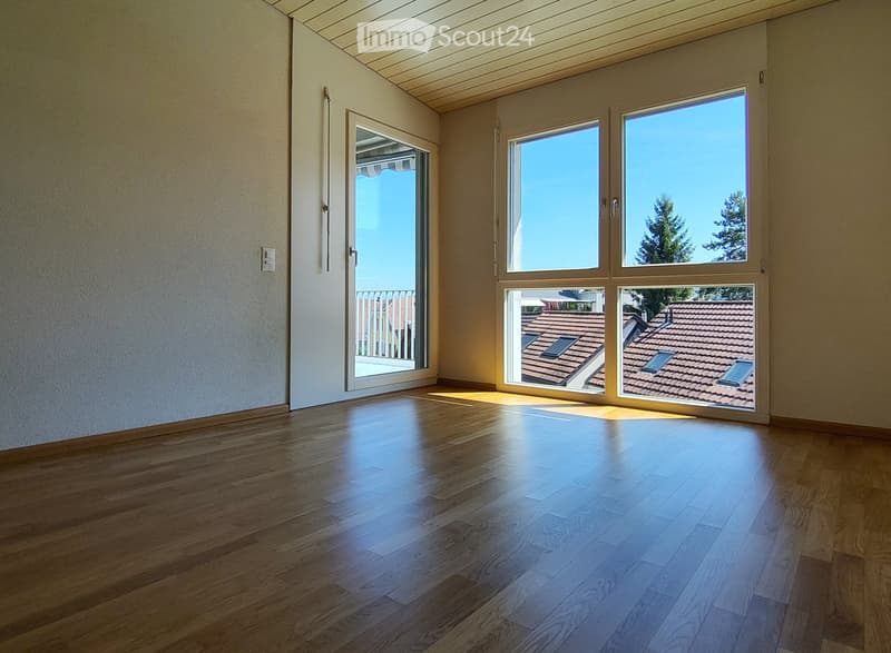 Empty room with wooden flooring, large windows, and a sliding door leading to a balcony.