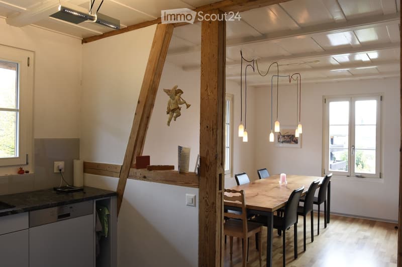 Open-plan kitchen and dining area with wooden beams, a dining table with chairs, a dishwasher, and pendant lights.