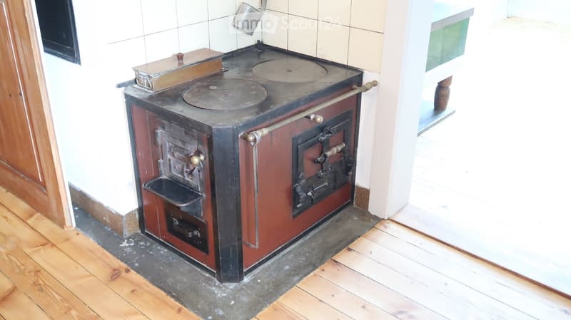 A vintage cast-iron stove with multiple burners and a large oven door, placed on a wooden floor in a tiled room.