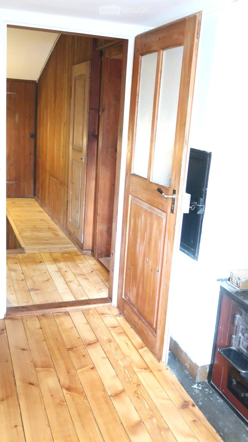 Empty wooden hallway with polished wooden floors, wooden doors, and white walls.