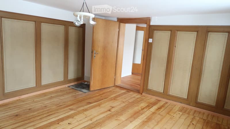 Empty room with wooden flooring, wooden panel walls, and a hanging light fixture. There are two open doors leading to other rooms.