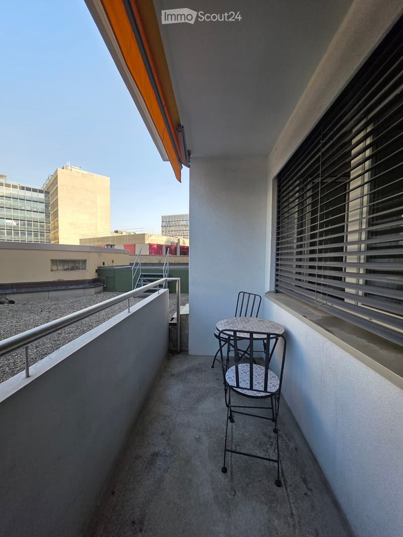 Balcony with a small round table and two chairs, metal railing, and an orange awning.