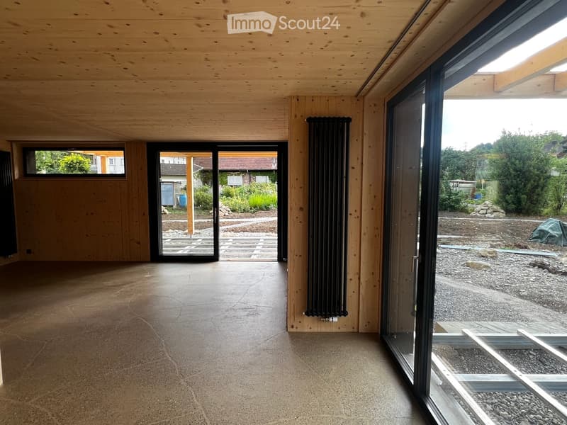 Empty room with wooden walls and ceiling, concrete floor, large sliding glass doors leading to outdoor area, radiator on wall.