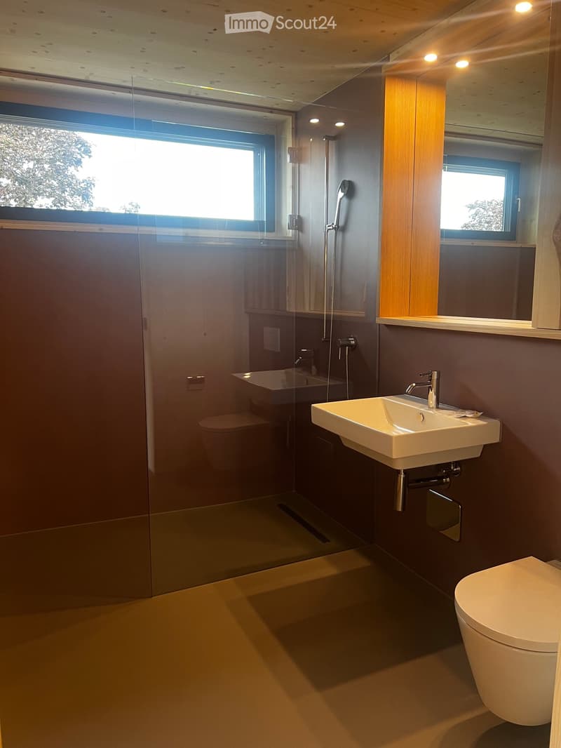 Modern bathroom with a white sink, chrome faucet, toilet, bathtub, and a glass-enclosed shower area. Features a large window and a mirror above the sink.