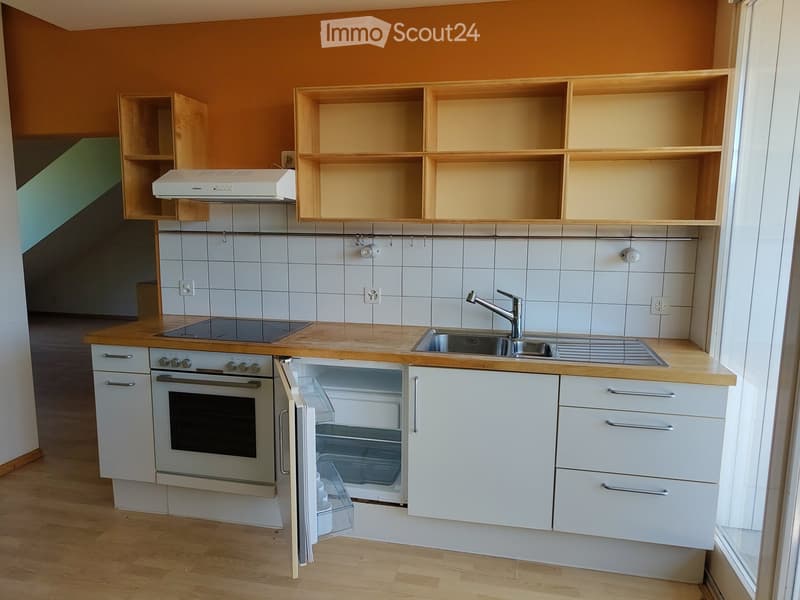 Modern kitchen with white cabinets, wooden countertops, stainless steel sink, oven, refrigerator, and range hood. The walls are tiled in white, and the floor is wooden.