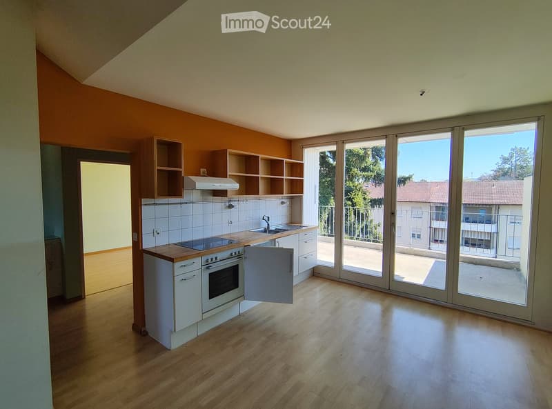 Modern kitchen with white cabinets, wooden countertops, and built-in appliances, featuring a large sliding glass door leading to a balcony.