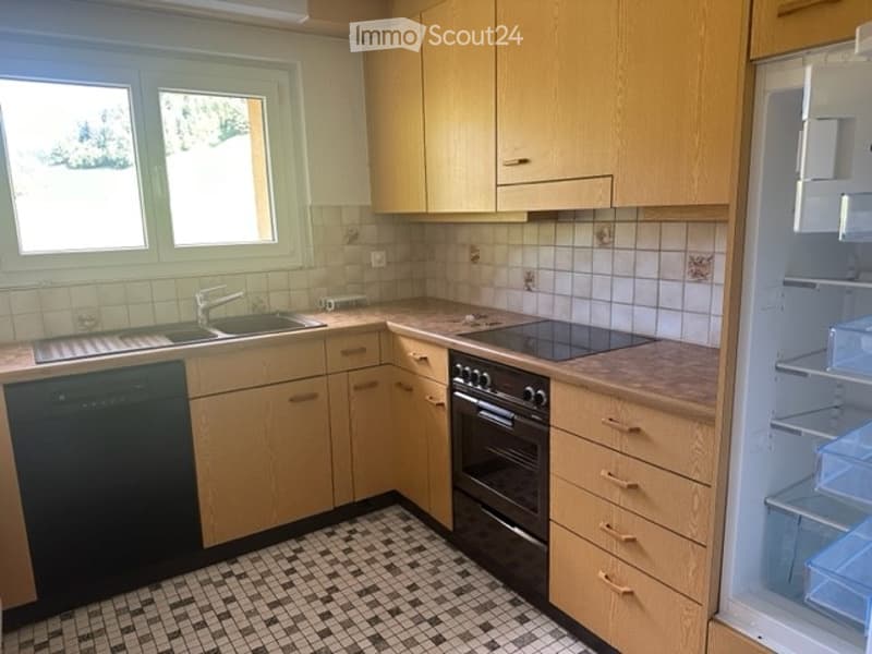 Bright kitchen with light wooden cabinets, tiled backsplash, and black appliances including a dishwasher, oven, and refrigerator. The space features a checkered tile floor and a window above the sink.