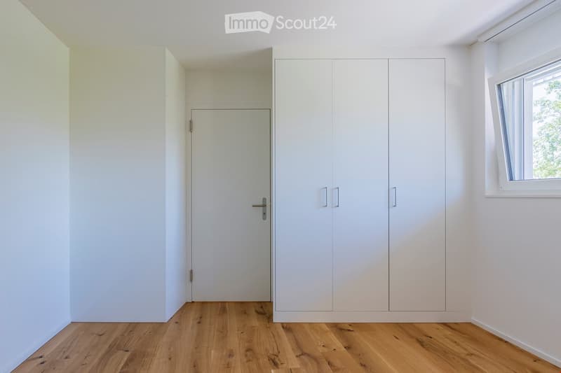 Empty room with white walls, wooden floor, window, and built-in wardrobes