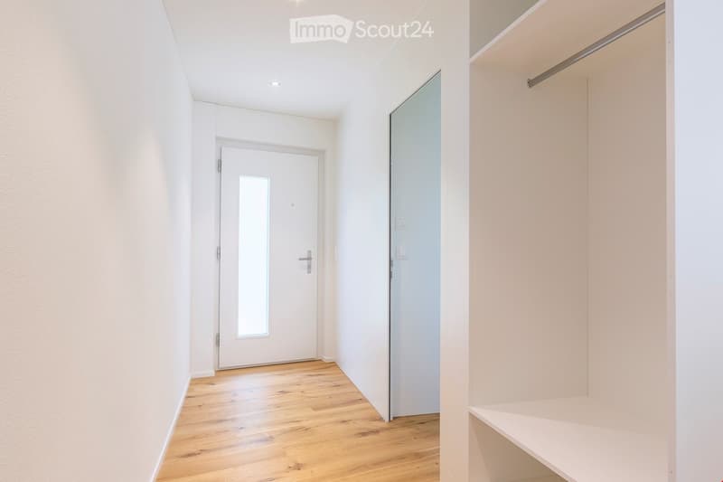 Empty hallway with wooden floor, white walls, glass door, closet