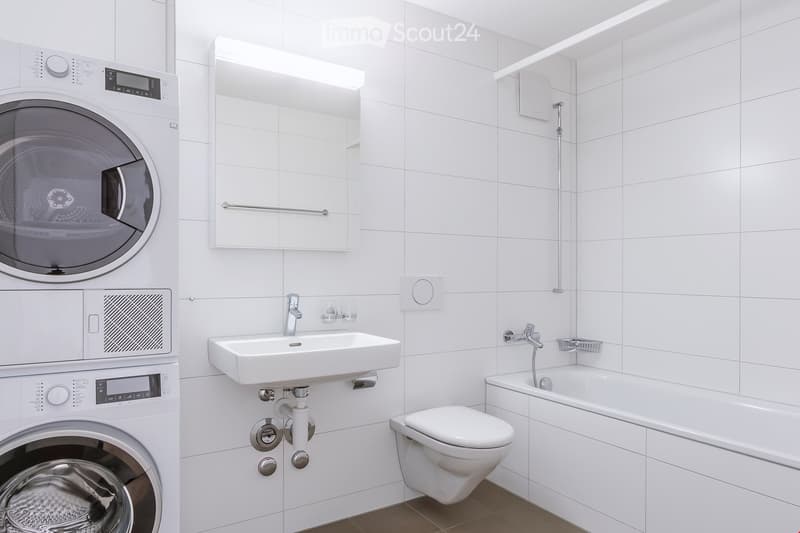 Modern, clean and white bathroom with washing machine, sink, toilet, bathtub and mirror