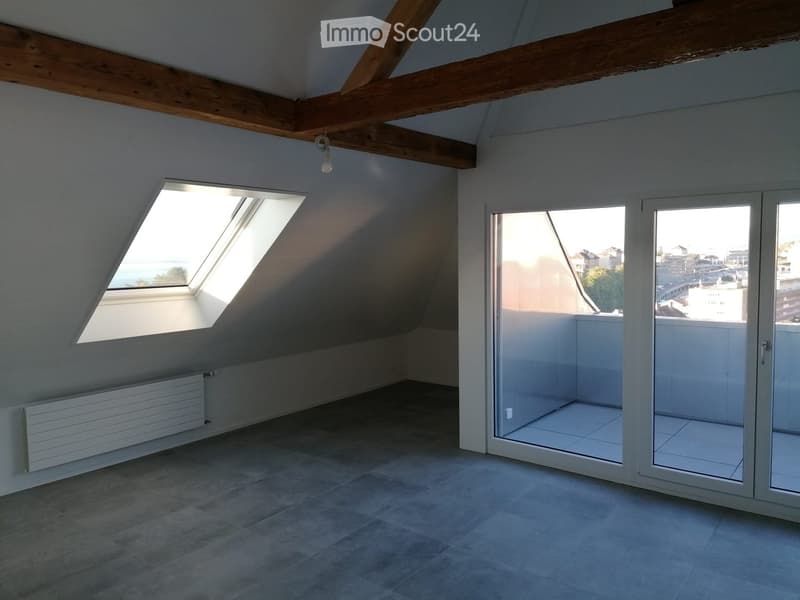 Empty attic room with exposed wooden beams, skylight windows, and large sliding glass doors leading to a balcony.