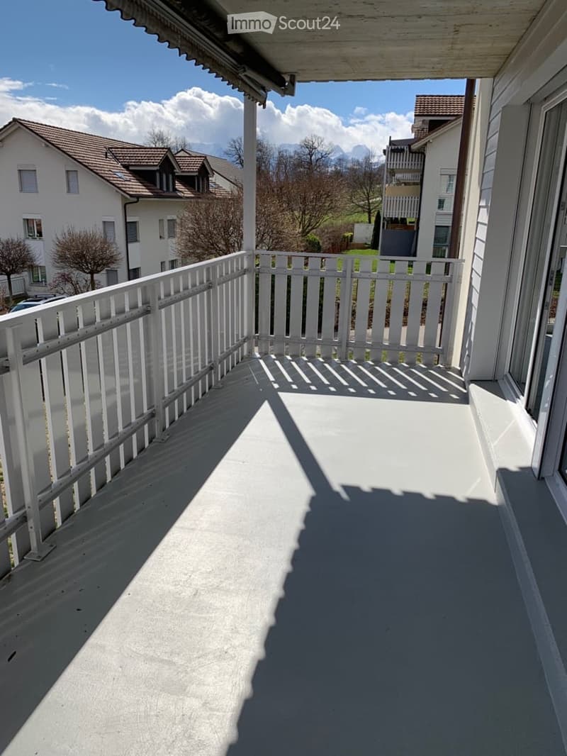 a balcony with white fence railings, a concrete floor and a view of the surrounding area