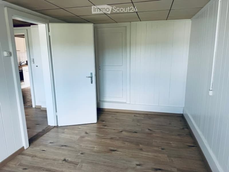 Empty room with wooden flooring, white walls, and a closed white door. No furniture or equipment is present.