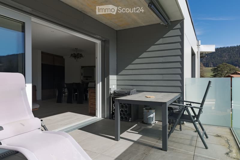 Balcony with a modern table, chairs, and a lounge chair, overlooking a scenic landscape.