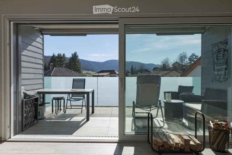 Balcony with a view of the mountains, featuring a table, chairs, a wine rack, and a stack of firewood.