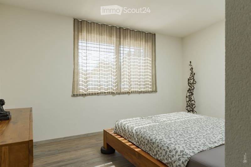 Minimalist bedroom with a wooden bed, nightstand, and decorative sculptures. Light-colored walls and wooden flooring.