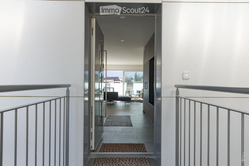 Modern hallway with white walls, metal railings, and a view into a living area with a sofa and coffee table.