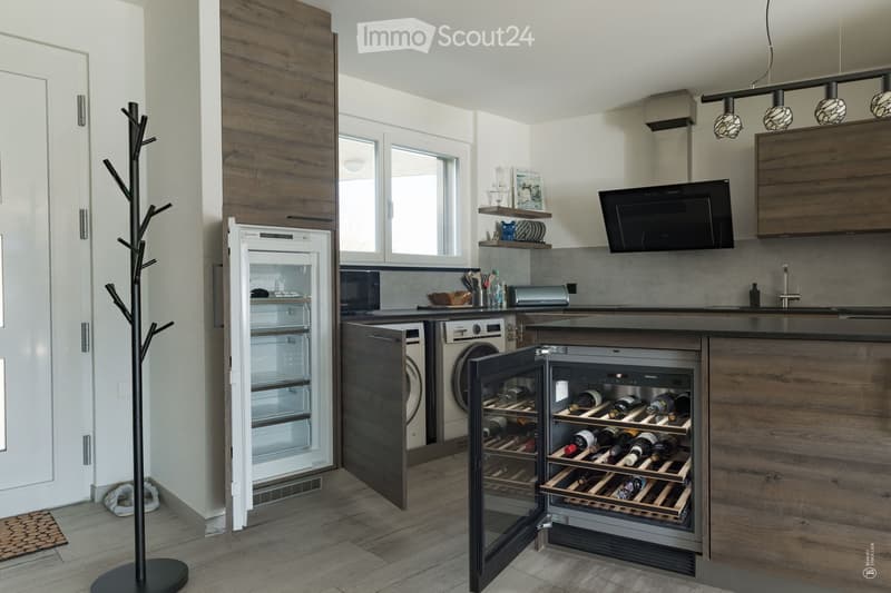 Modern kitchen with wooden cabinets, stainless steel appliances, a wine cooler, and a refrigerator. The space features a sleek design with a central island and ample storage.
