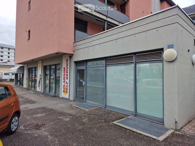 Modern commercial building with glass storefront and signage reading "SOLARIUM SELF SERVICE." Features a raised entrance, concrete facade, and adjacent parking area.