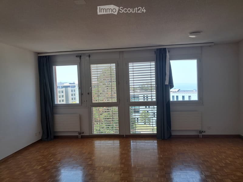 Empty room with wooden flooring, large windows with blinds, and radiators. No furniture or personal items present.