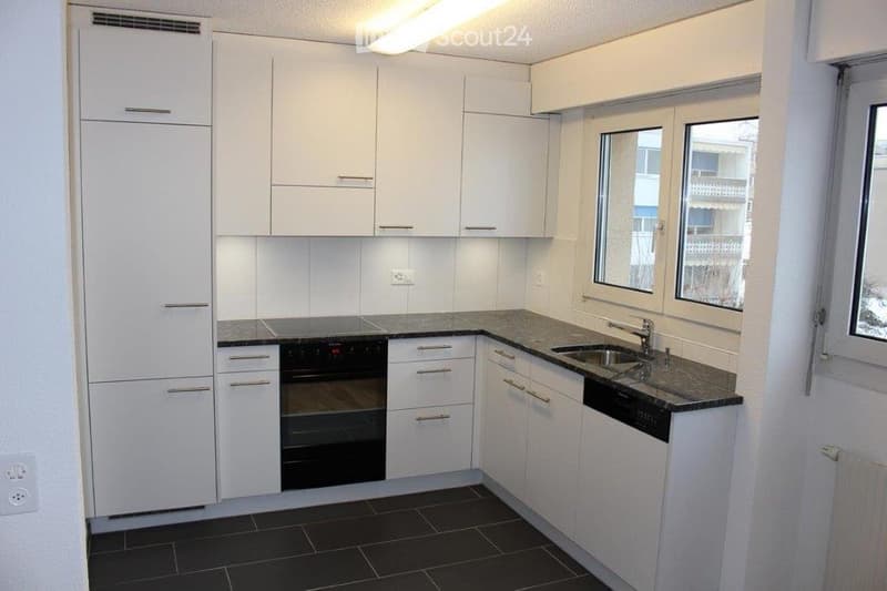 Modern kitchen with white cabinets, black countertops, and stainless steel appliances including a refrigerator, oven, and sink.