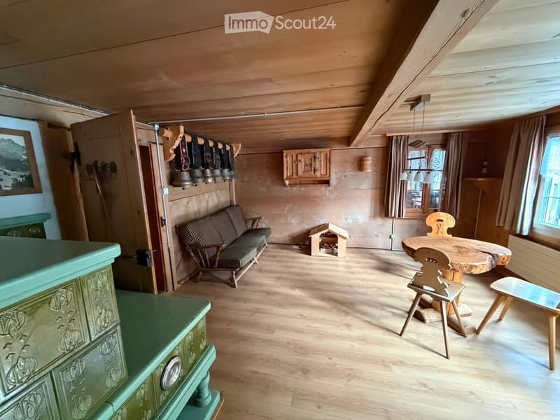 Cozy living room with wooden beams, a green cabinet, a sofa, a wooden table with chairs, and a small dog house.