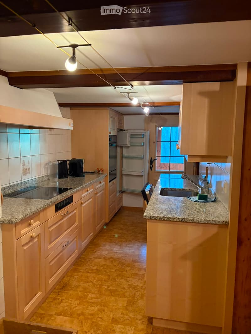 A well-lit kitchen with light wooden cabinets, granite countertops, and a tiled backsplash. Features include a refrigerator, oven, sink, and various kitchen appliances.