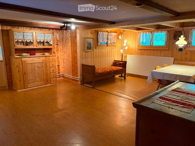 Cozy room with wooden walls and floor, featuring a wooden cabinet, a small sofa, a dining table with chairs, and a floor lamp.