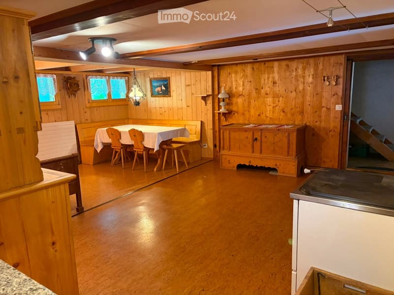 Cozy wooden-paneled room with a dining area featuring a table and chairs, a wooden cabinet, and a small lamp on a shelf.