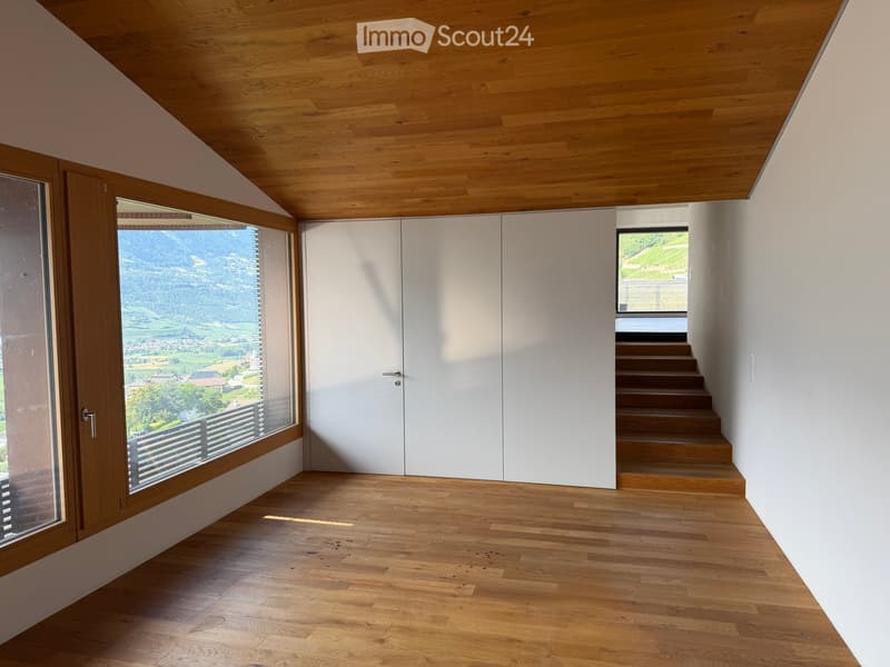 Bright hallway with wooden flooring and ceiling, large windows offering scenic views, white cabinetry, and a staircase leading upwards.