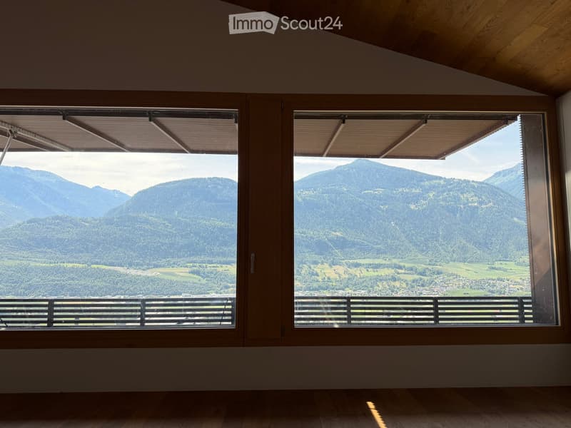 Empty room with large windows offering a scenic mountain view, wooden floor, and simple wooden window frames.