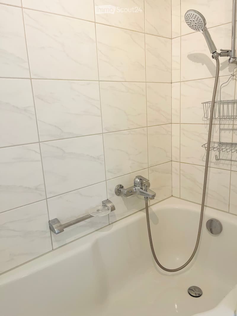 Bathtub with modern chrome fixtures, including a handheld showerhead and a fixed faucet, surrounded by marble tiles.