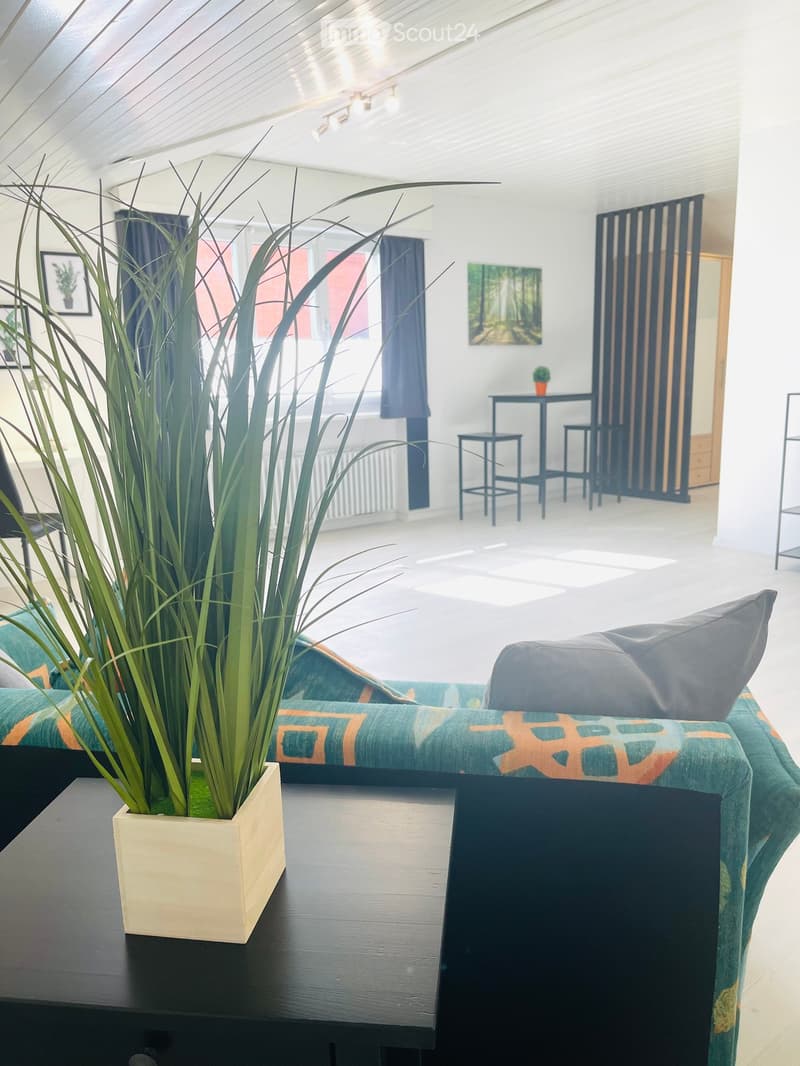 Modern living room with a green sofa, black coffee table, tall potted plant, and a small bar area with stools.