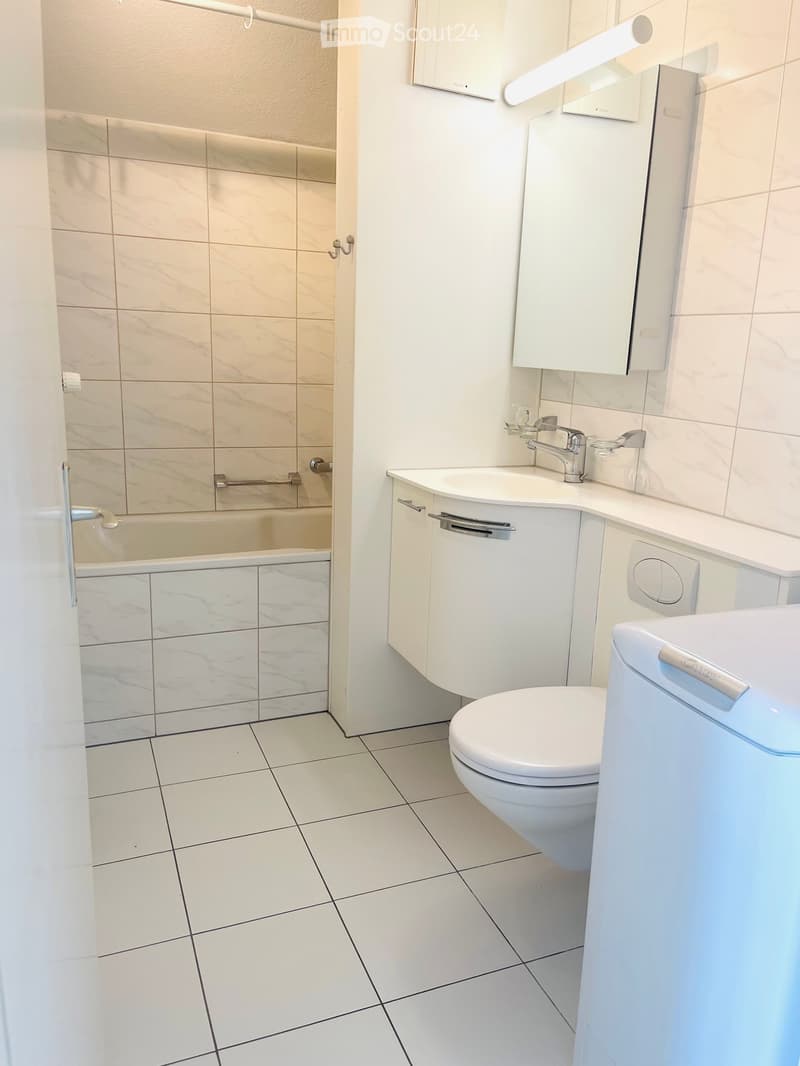 Modern bathroom with white tiles, a toilet, a sink with a faucet, a mirror, and a bathroom cabinet.