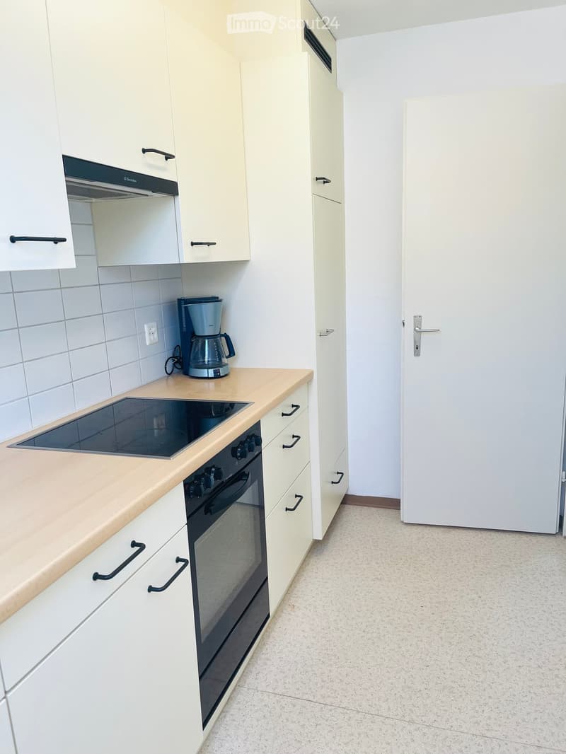 Modern kitchen with white cabinets, light wooden countertops, an induction stove, and a coffee maker on the counter.