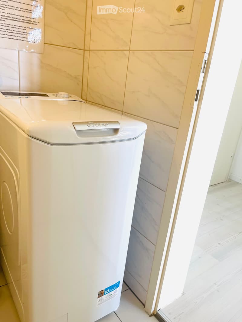 Bathroom with a white washing machine, beige tiled walls, and a partially visible wooden floor.