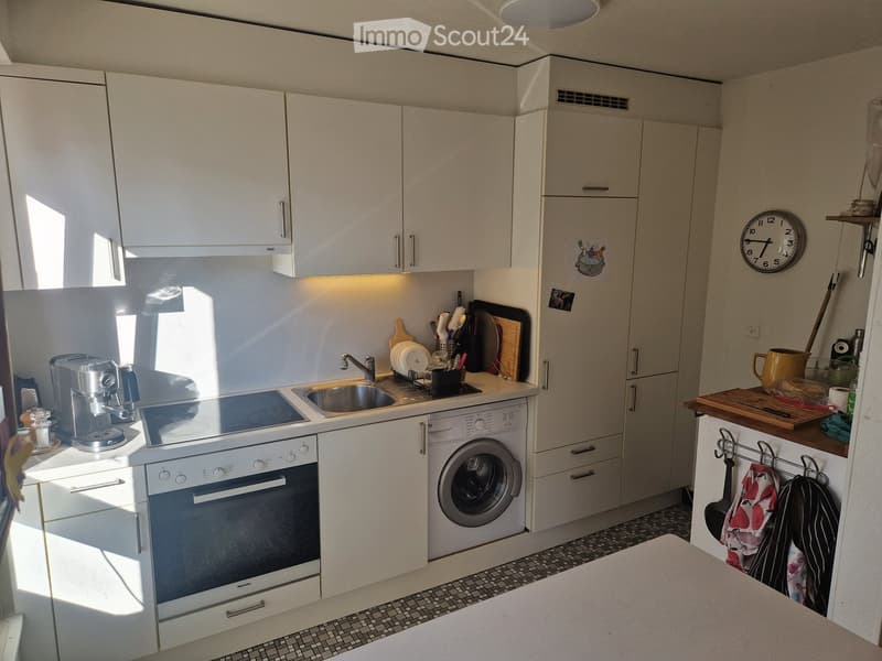 Modern kitchen with white cabinets, stainless steel appliances, and a tiled floor. Features include an oven, washing machine, coffee maker, sink, and various kitchen utensils.