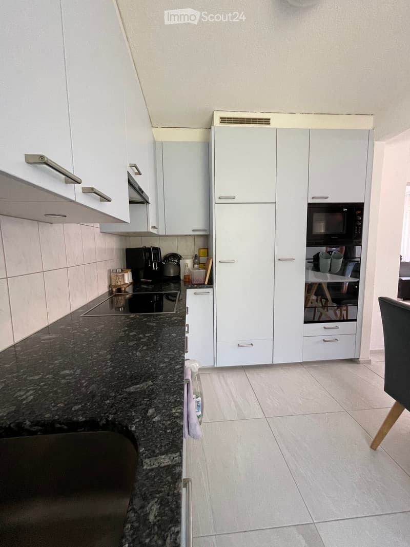 Modern kitchen with white cabinets, granite countertop, built-in oven, microwave, and coffee maker. Features a tiled backsplash and tiled floor.