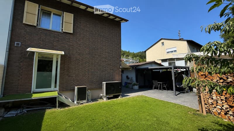 Garden with green artificial turf, patio area with furniture, outdoor dining setup, and a stack of firewood.