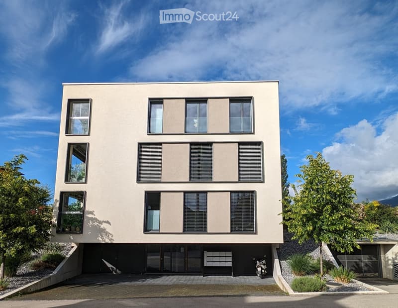Modern two-story house with beige facade, large windows, and a raised ground floor with a garage entrance.