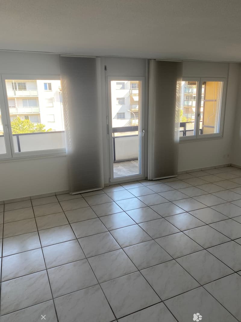 Empty room with tiled floor, large windows, and sliding glass door leading to a balcony.
